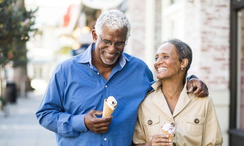 older couple walks down city sidewalk while holding ice cream cones